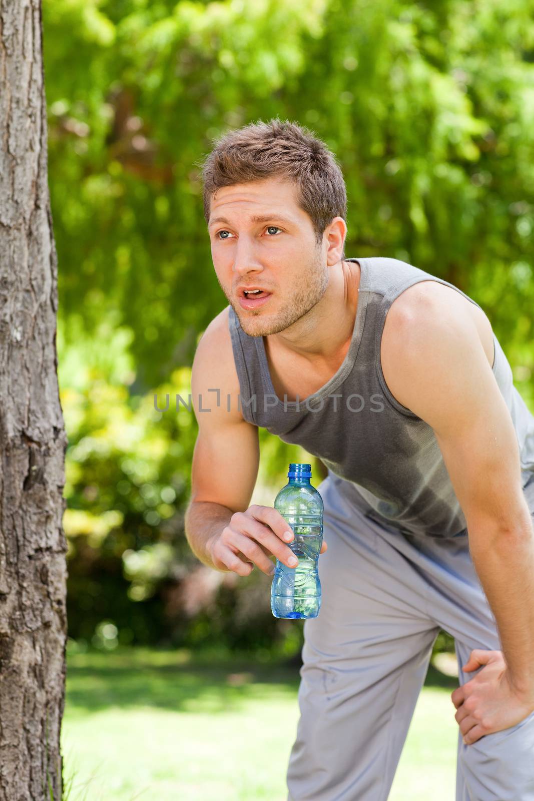 Sporty man drinking water in the park during the summer