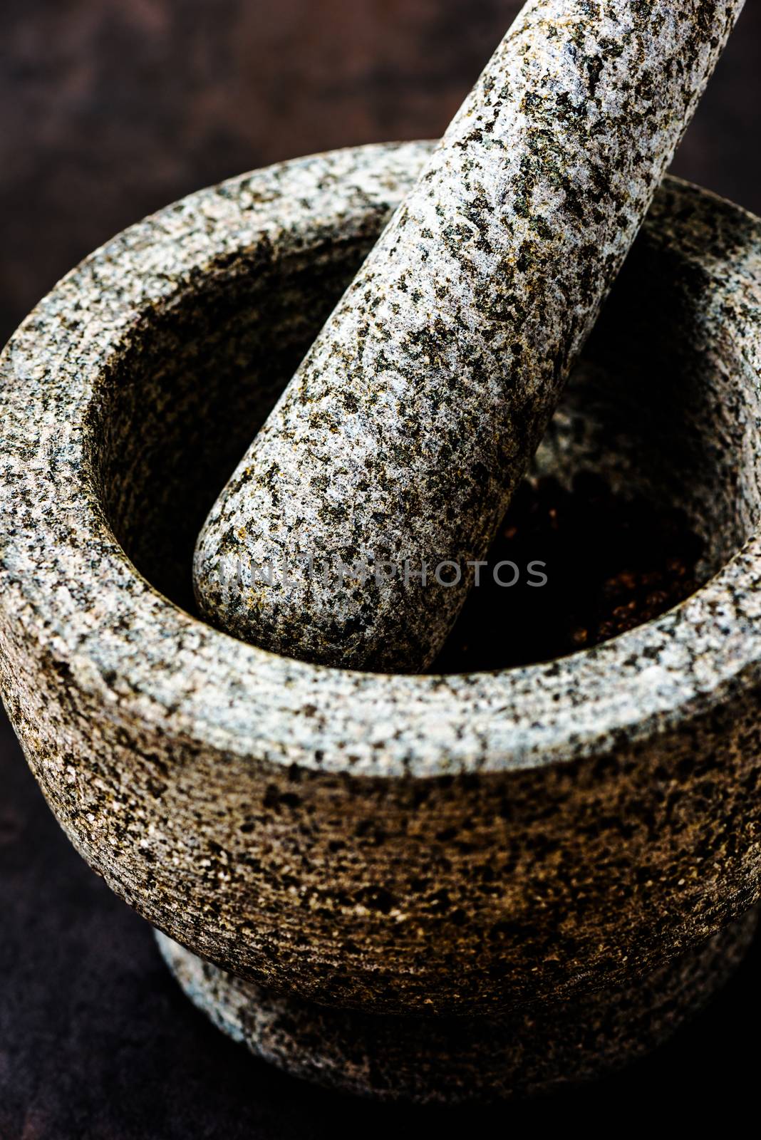 Stone mortar bowl and pestle on dark stone surface by Nanisimova