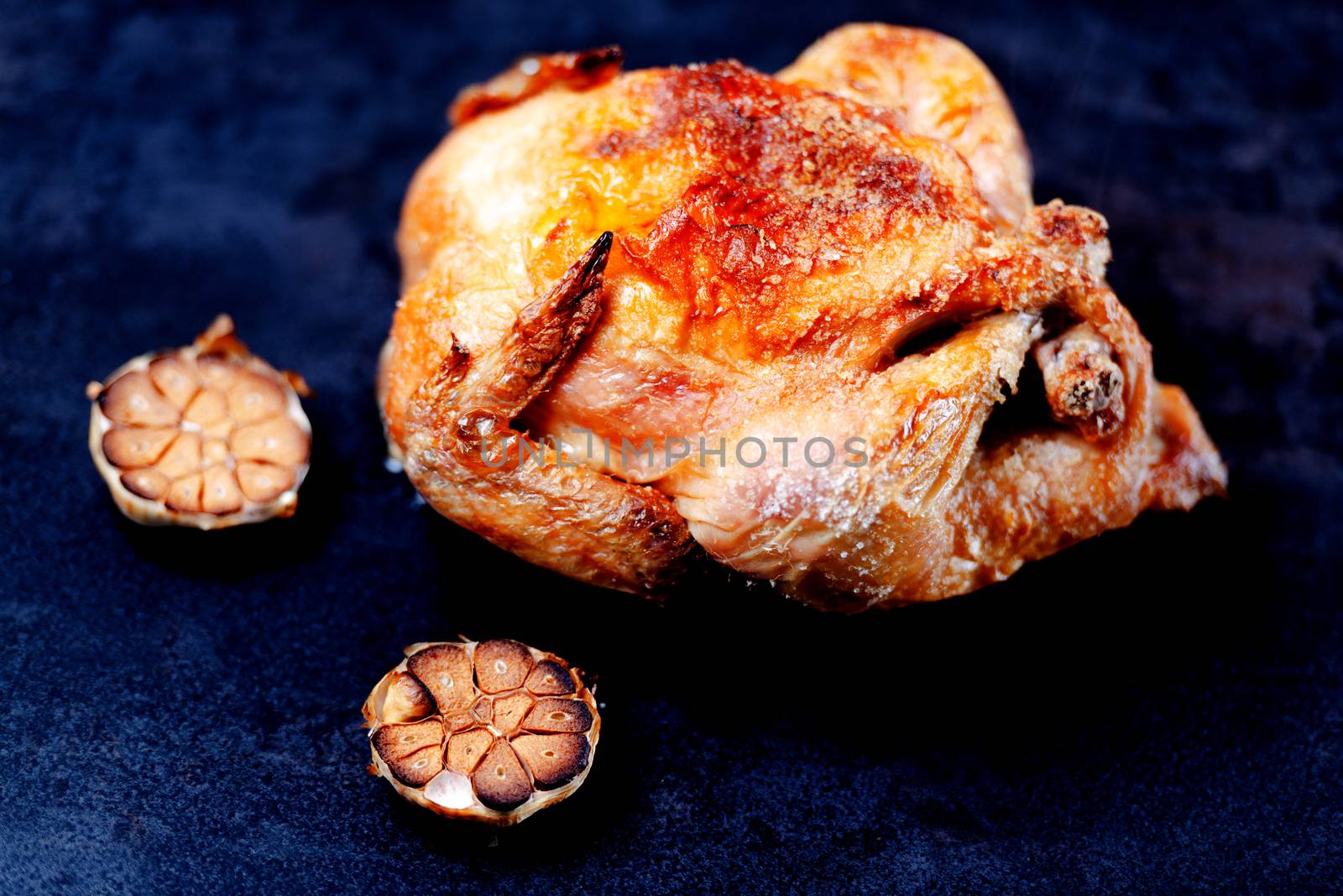Whole oven roasted chicken with garlic on stone surface