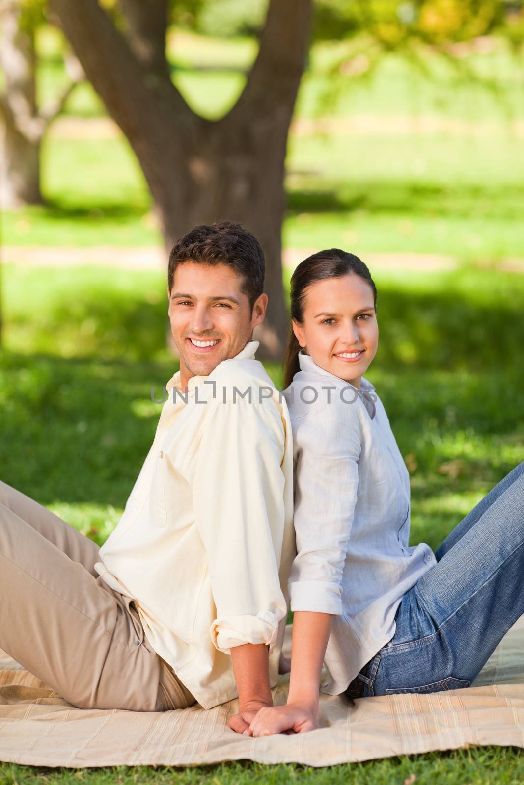 Couple sitting back-to-back in the park during the summer