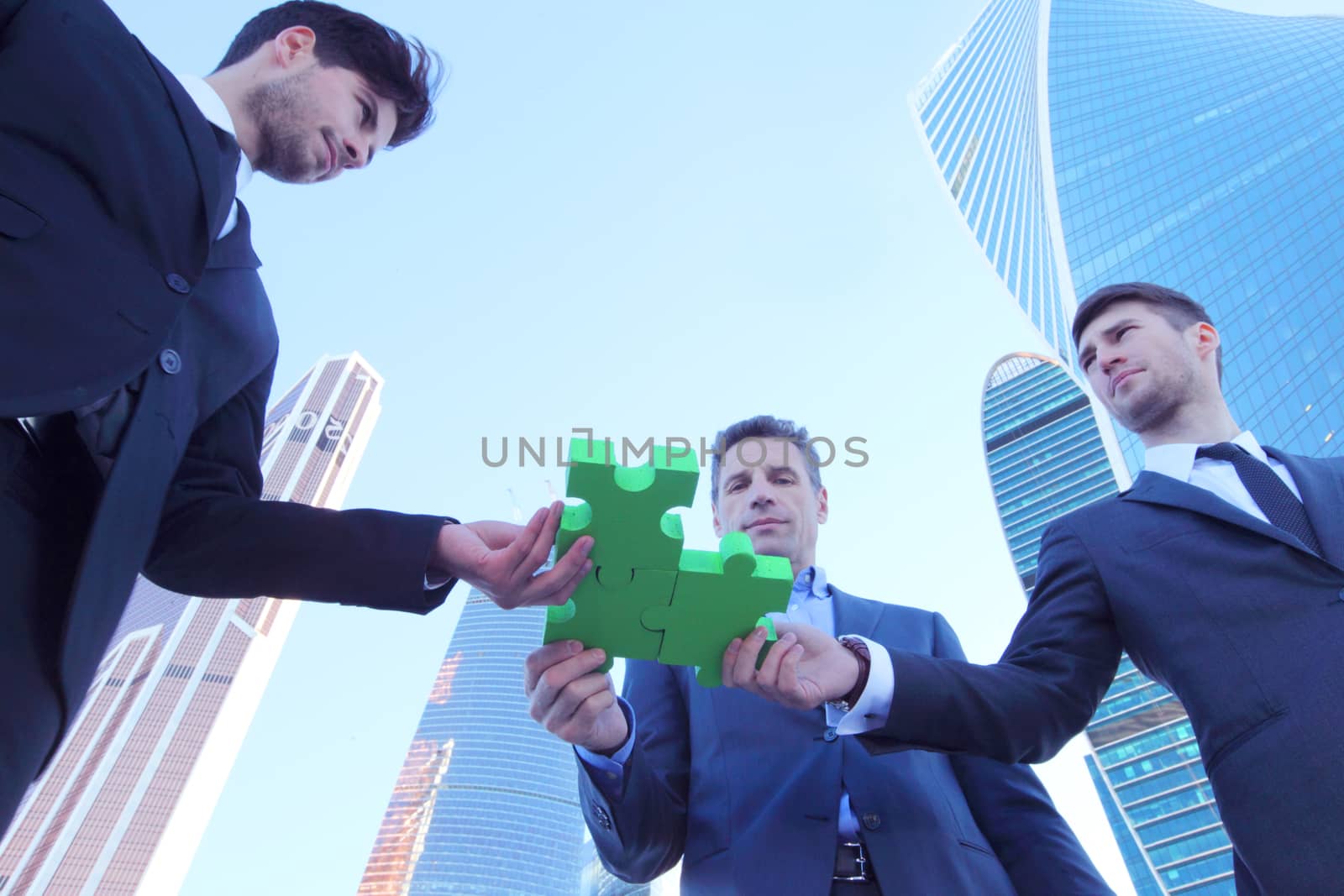 Business people assembling jigsaw puzzle near skyscrapers