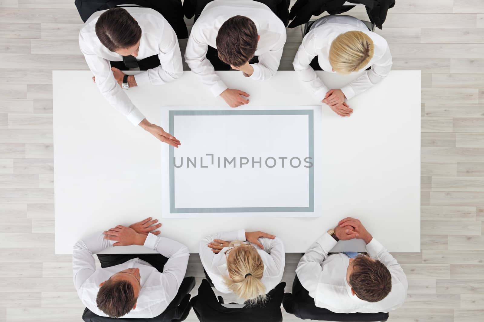 Business people sitting around empty table, business man pointing to blank copy space in the middle