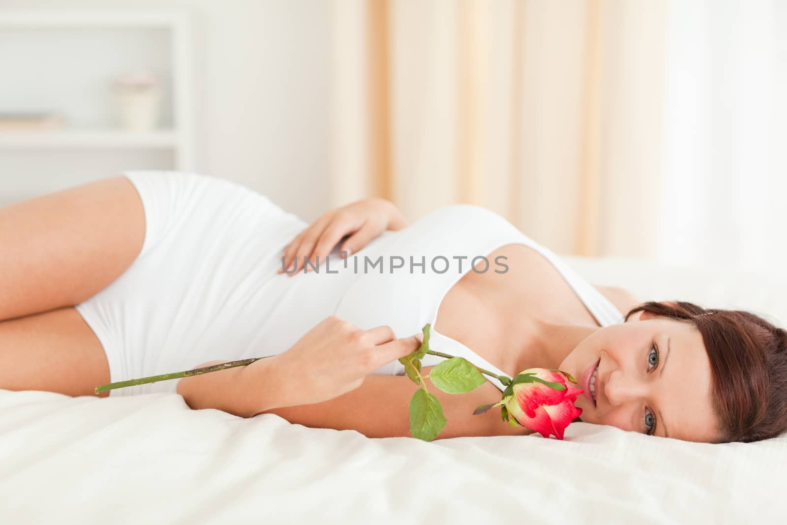 Young Woman with a rose looking into camera in her bedroom