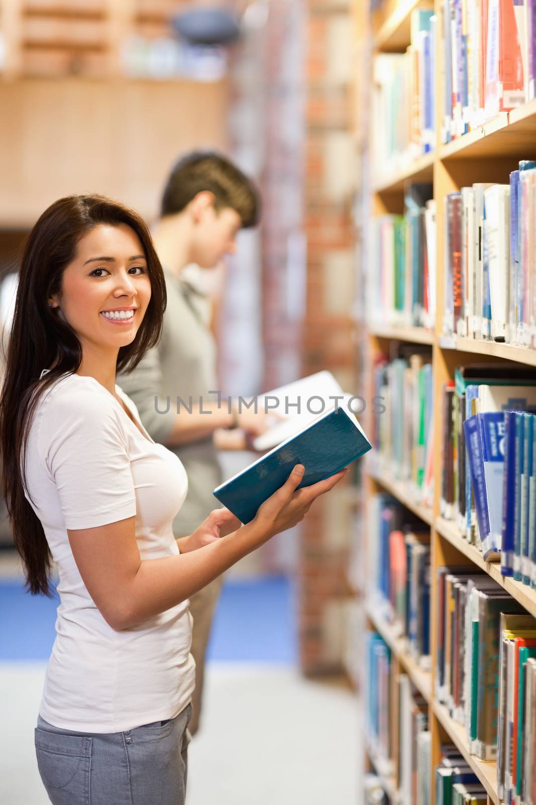 Portrait of a brunette student holding a book while looking at the camera