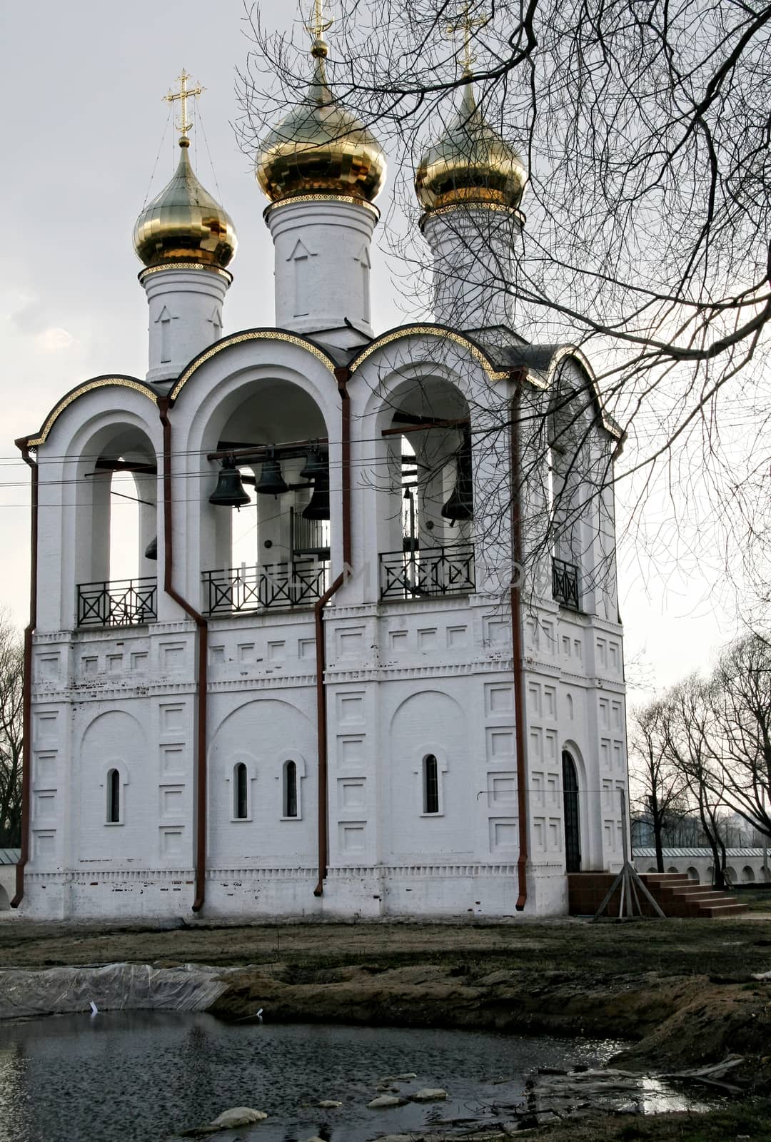 White orthodox church with a golden dome on a background of tree branches in early spring