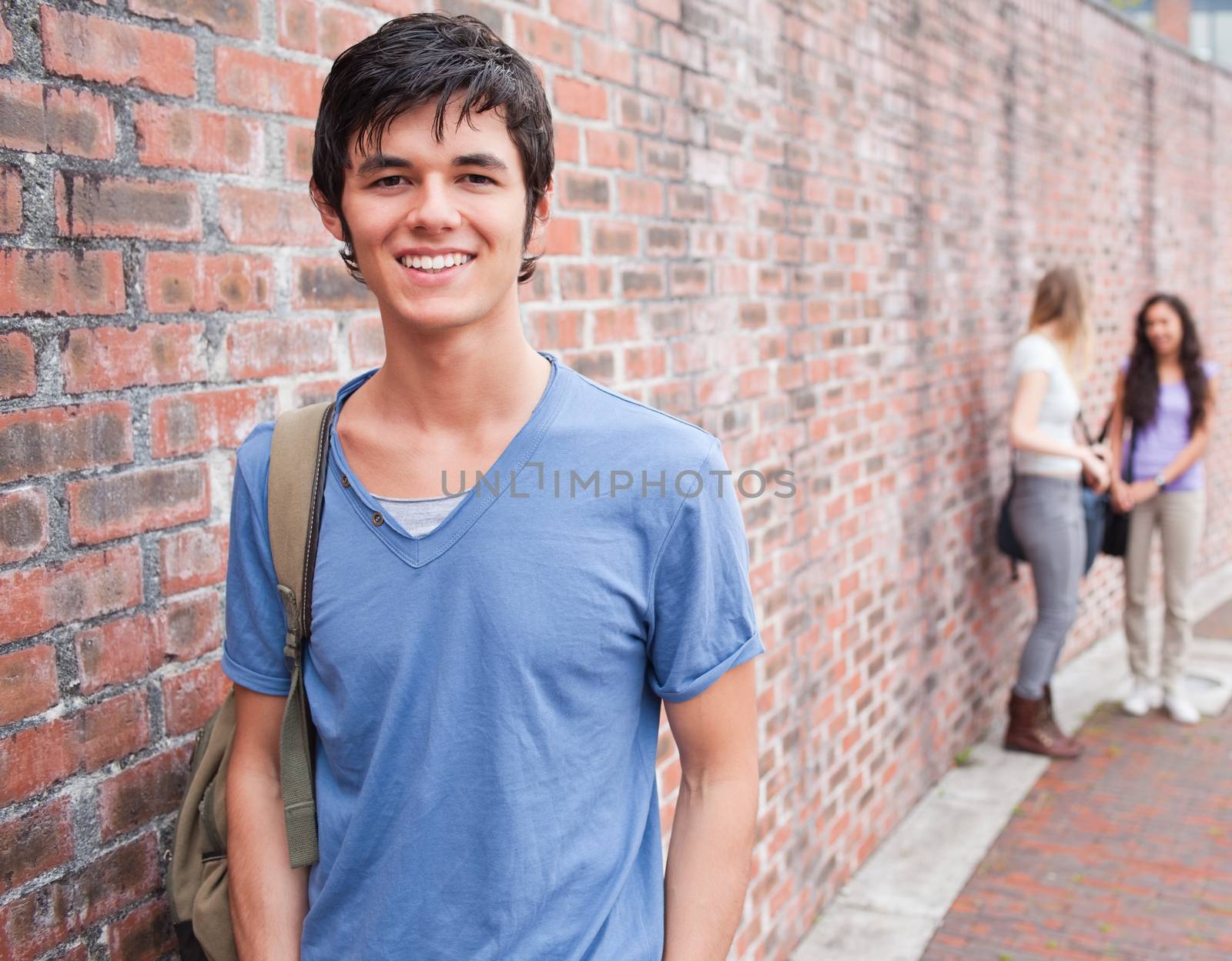 Handsome student posing while his friends are talking outside a building