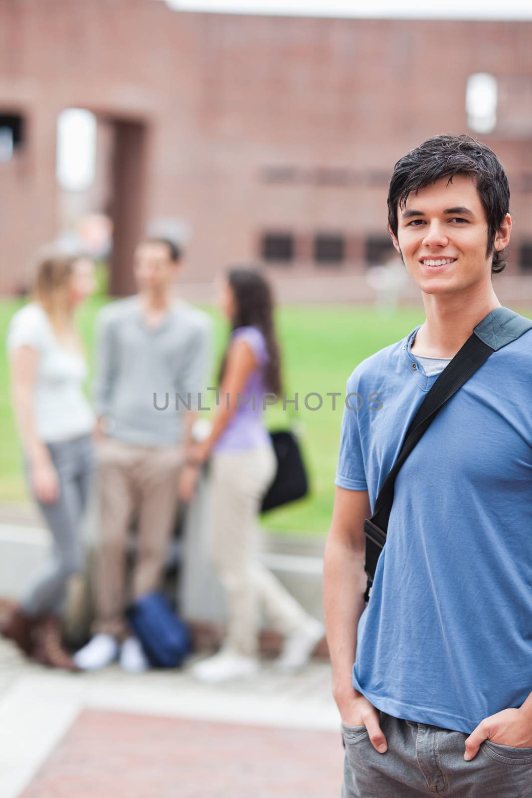 Portrait of a handsome student posing while his classmates are talking by Wavebreakmedia