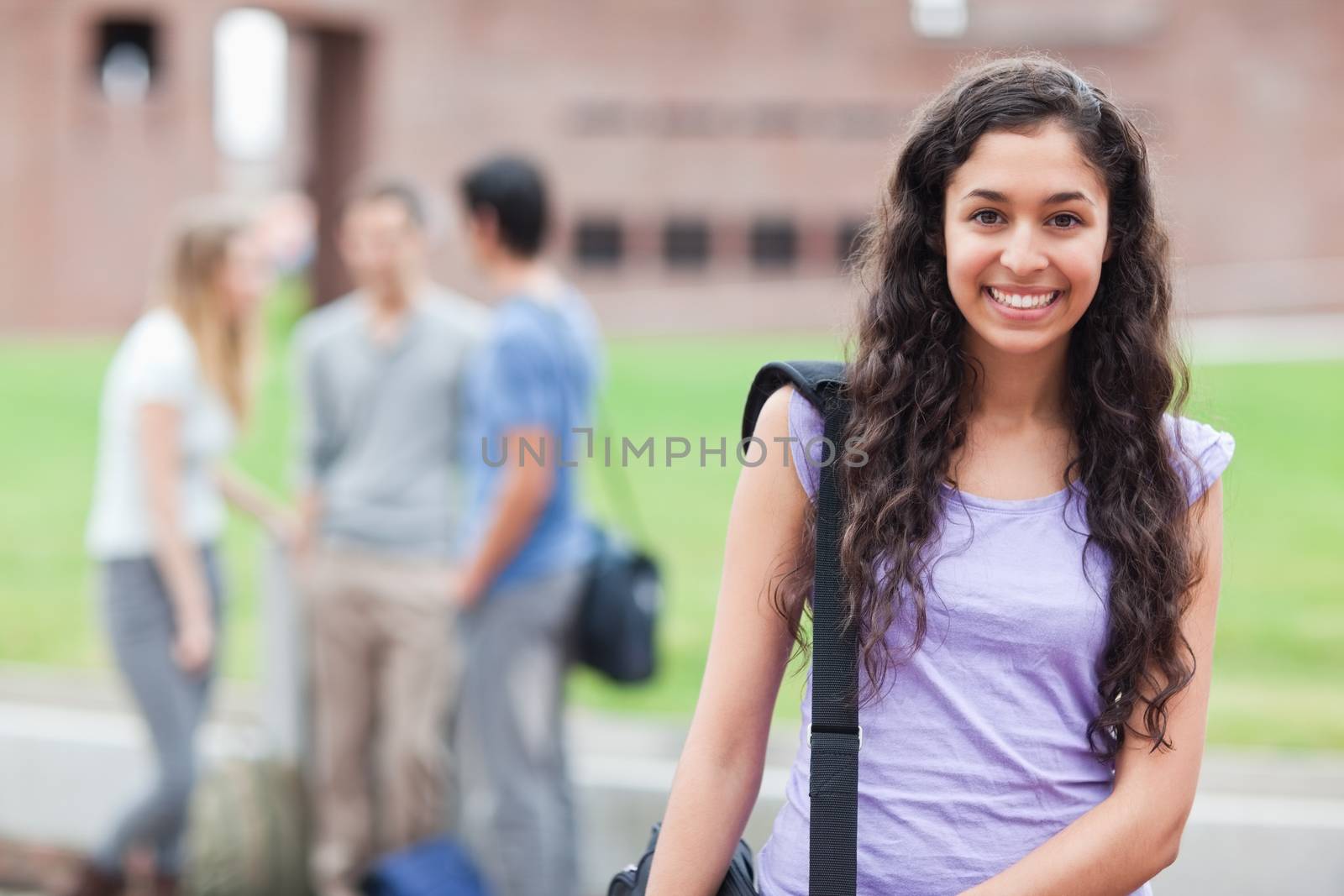 Cute student posing while his classmates are talking in a yard