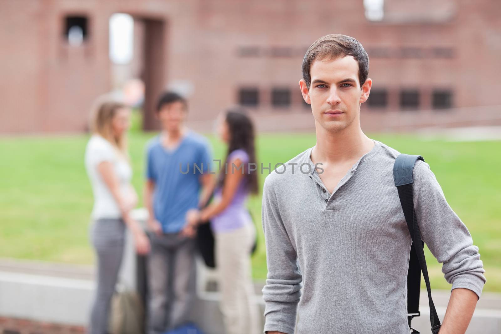 Male student posing while his classmates are talking in a yard
