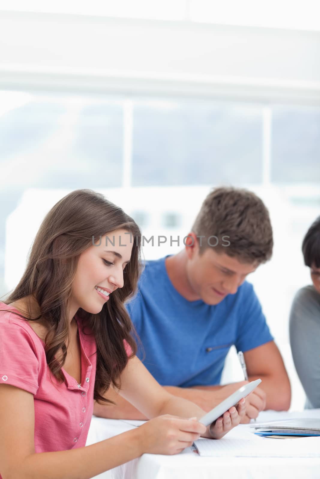 A close up shot of a smiling girl using her tablet pc with her friends studying beside her 