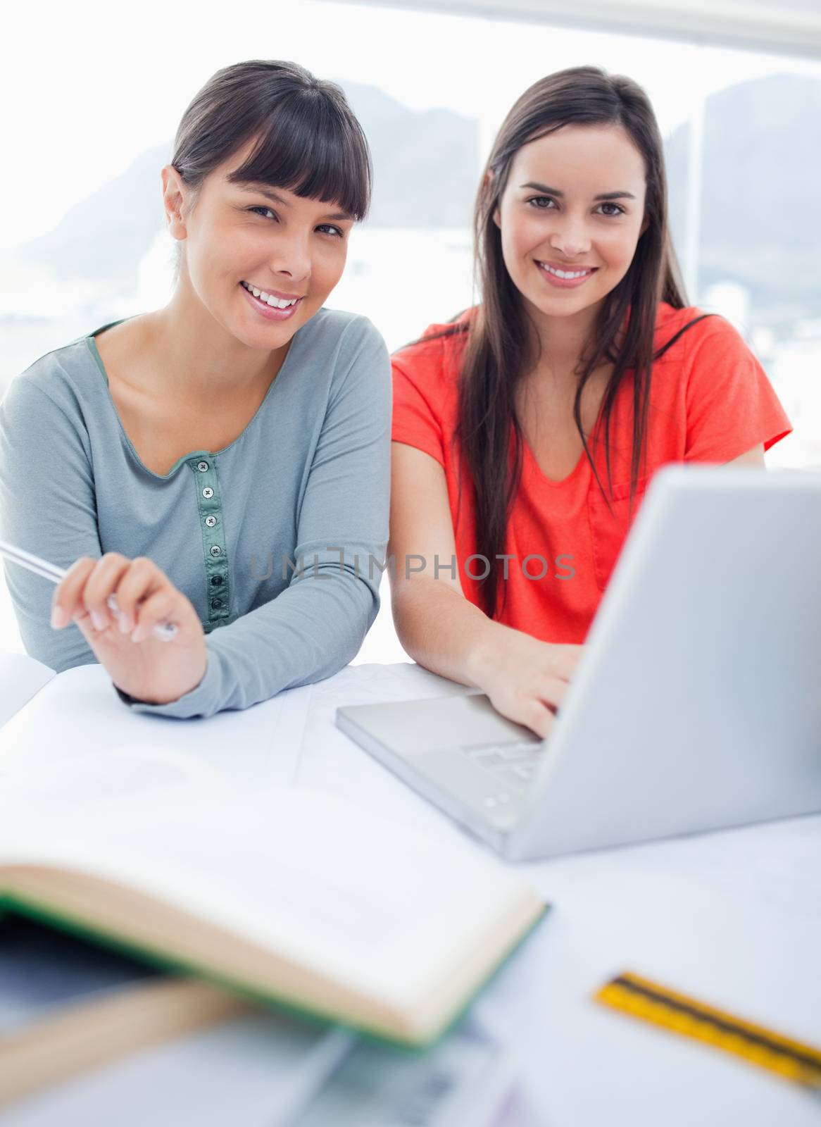 Close up shot of a girl and her friend smiling as they sit with a laptop by Wavebreakmedia