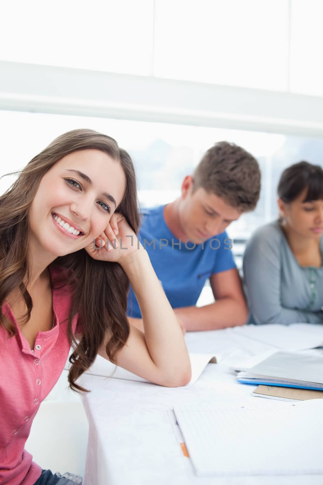 A smiling woman beside her friends looking into the camera with her head resting on her hand