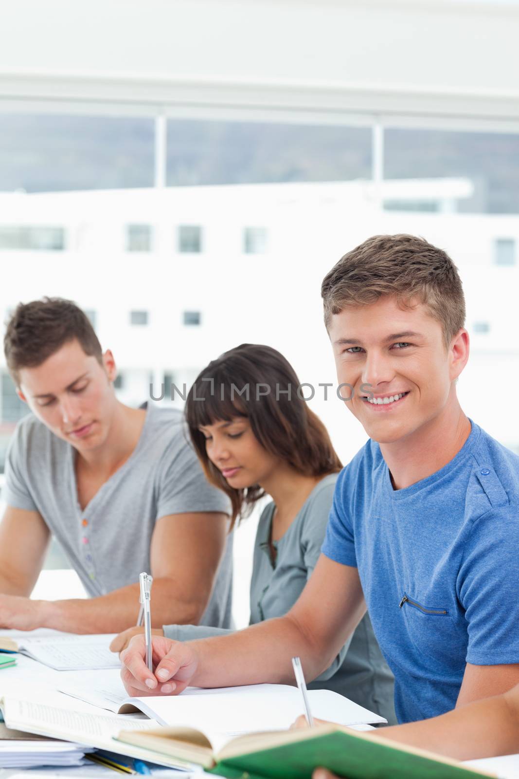 A smiling man looking into the camera while his friends work 