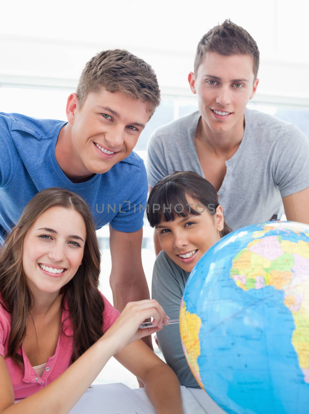 A smiling group of people sitting beside a globe as they look into the camera