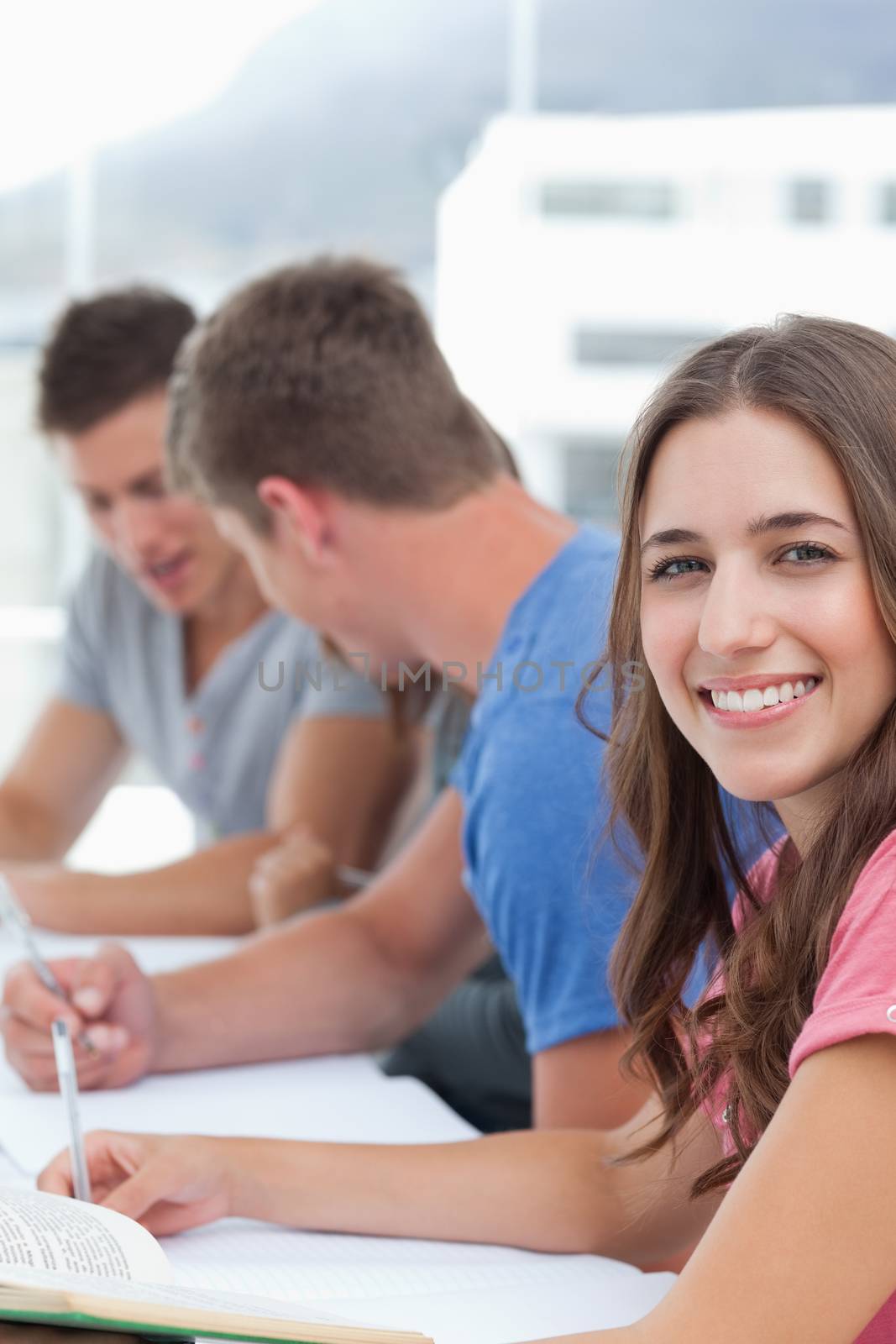 Close up of a woman smiling into the camera as the other people study by Wavebreakmedia