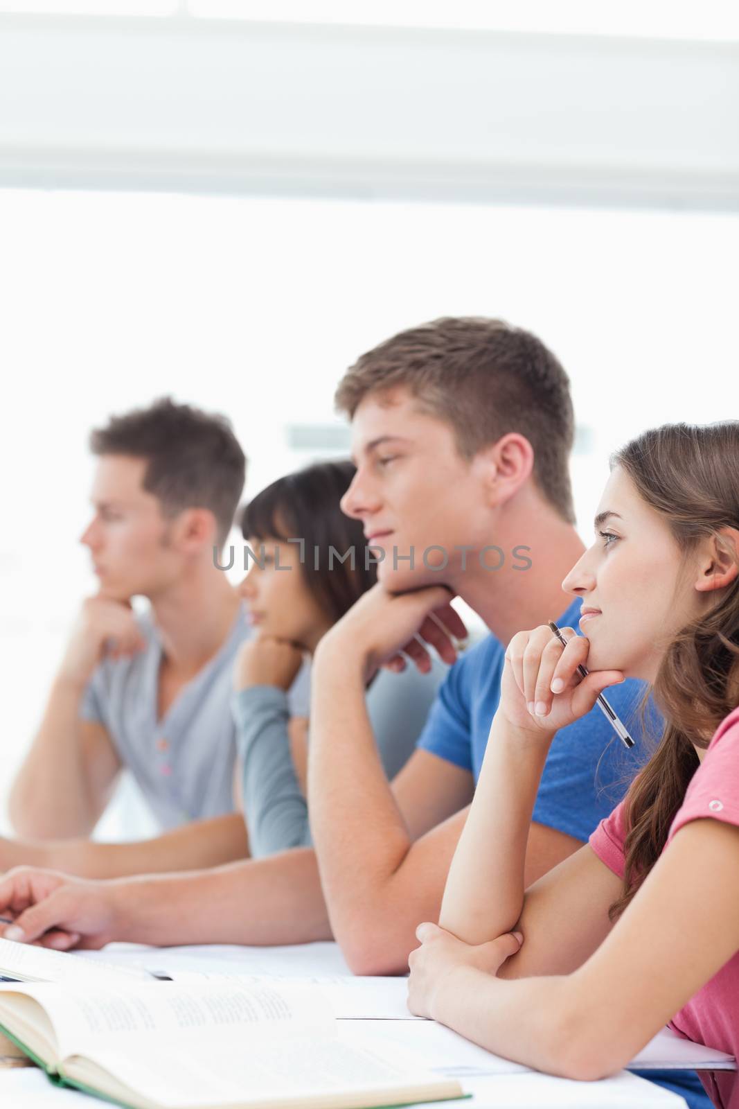 Four students listening in class while one looks tired by Wavebreakmedia