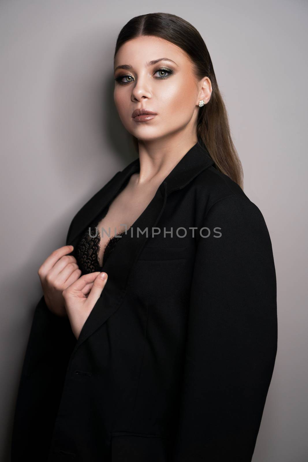 Beautiful young white girl close-up in a black jacket on a gray background. Make-up artist, beauty salon, stylist, magazine
