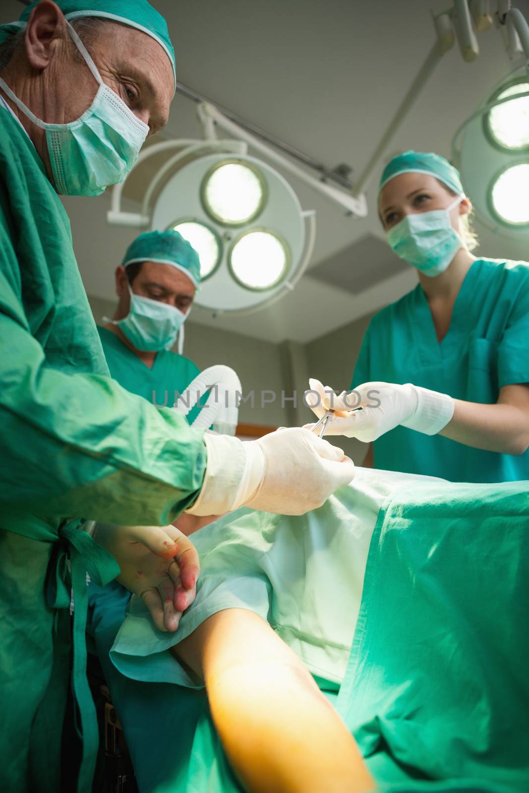 Team of surgeons operating the arm of a patient by Wavebreakmedia