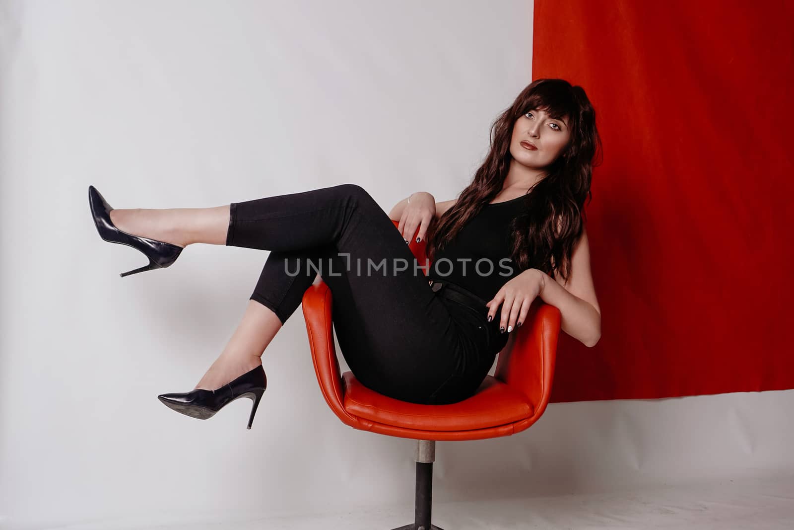 Young beautiful girl in business suit, shoes sitting on red chair, white background, business lady, young cute brunette