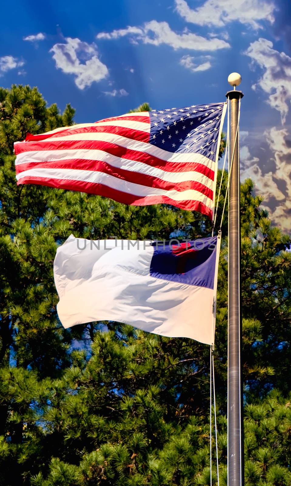 The Christian and American flags flying together against a background of trees and blue sky