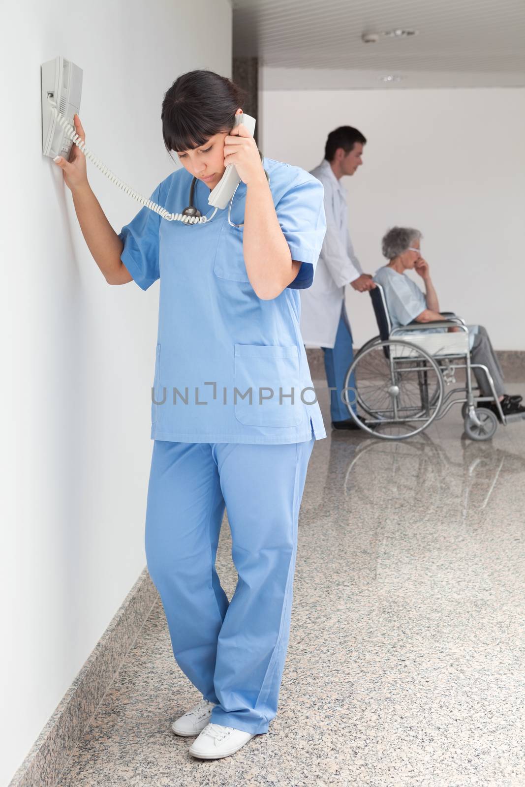 Nurse on telephone in hallway while doctor pushes patient in wheelchair