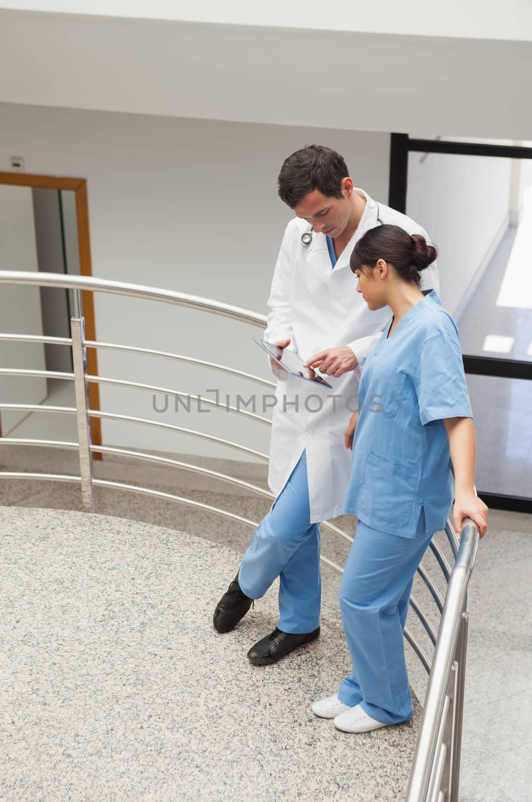 Nurse and doctor standing in the hallway and discussing with tablet pc