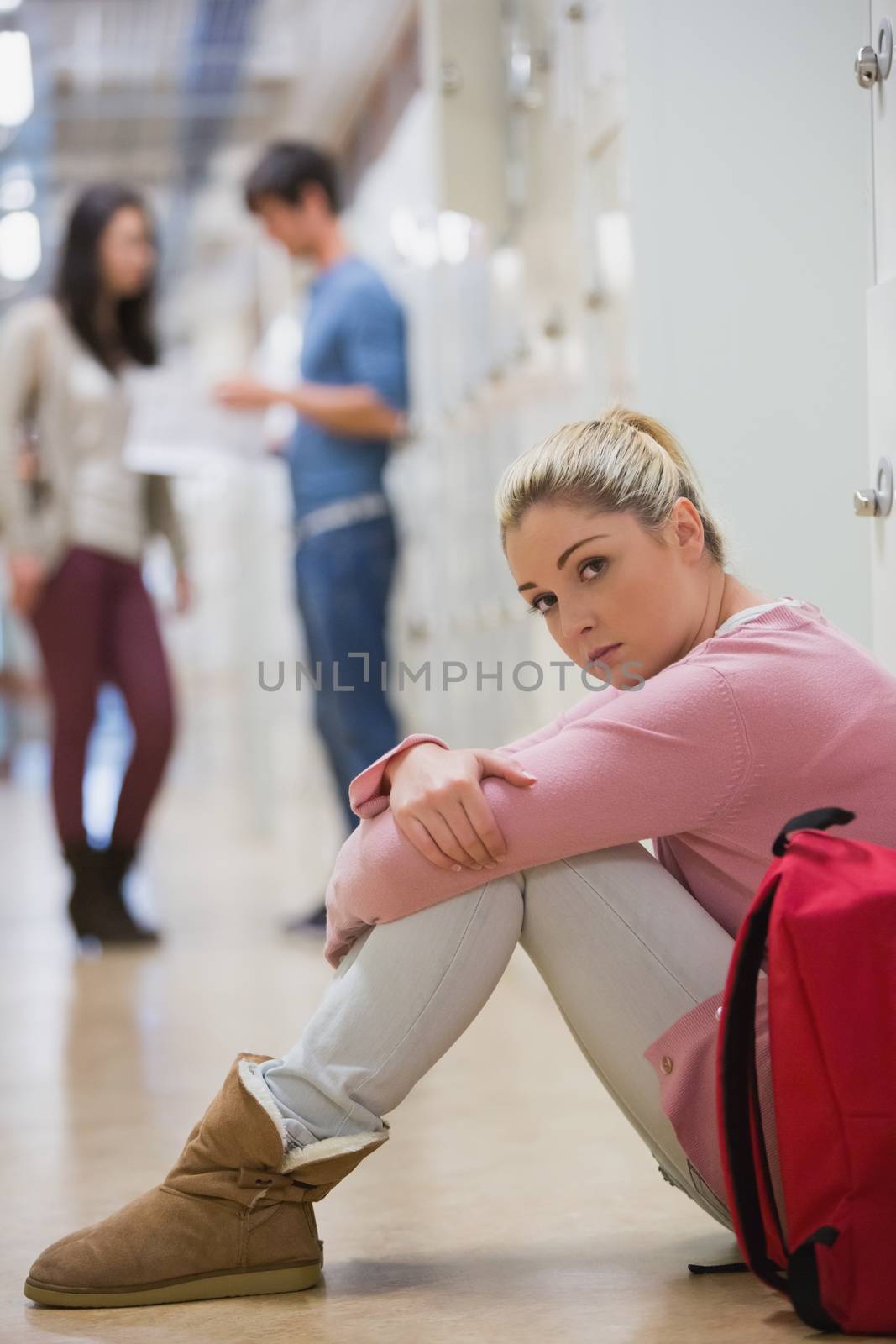 Sad student sitting on floor of college hallway against lockers