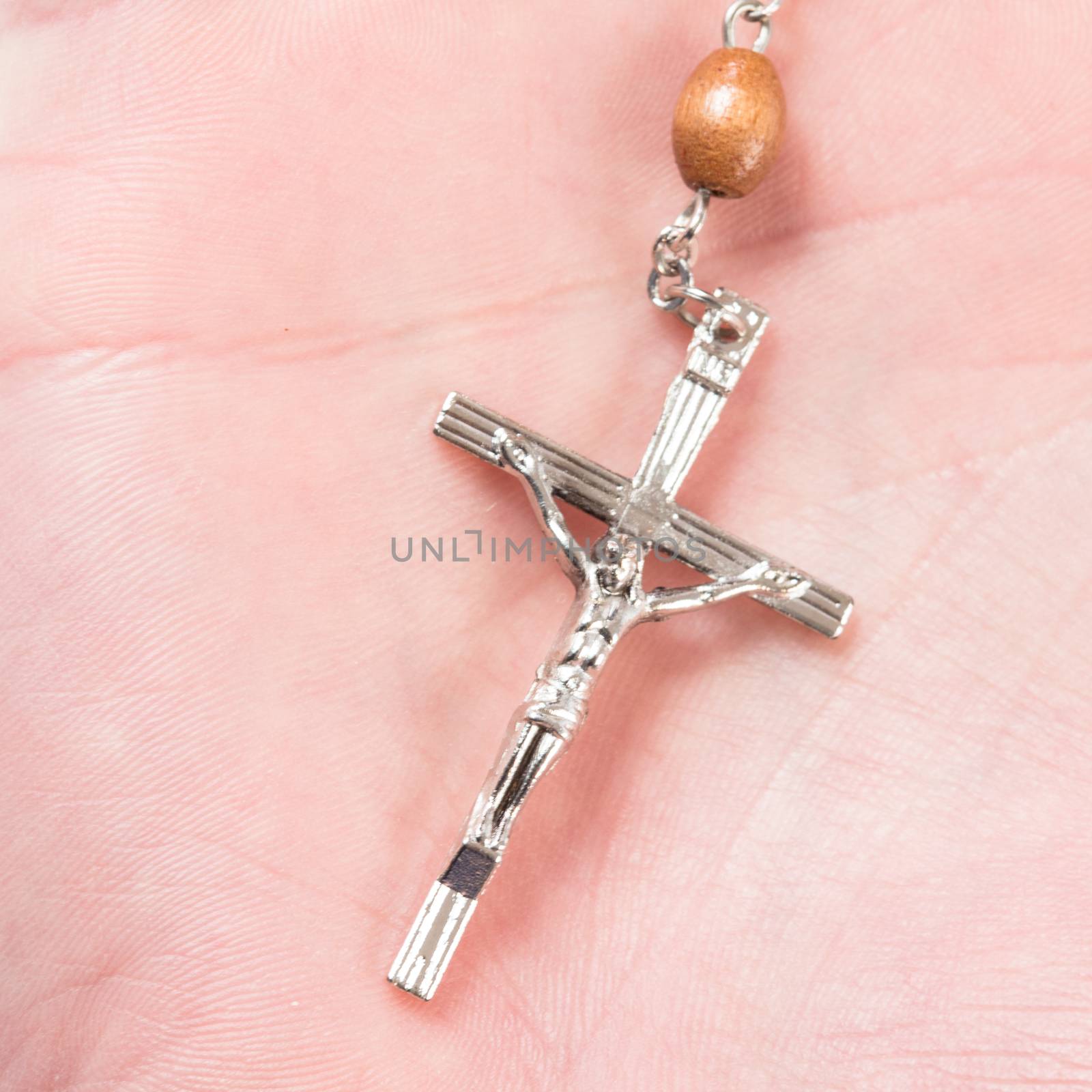 Silver cross of rosary beads in palm of hand