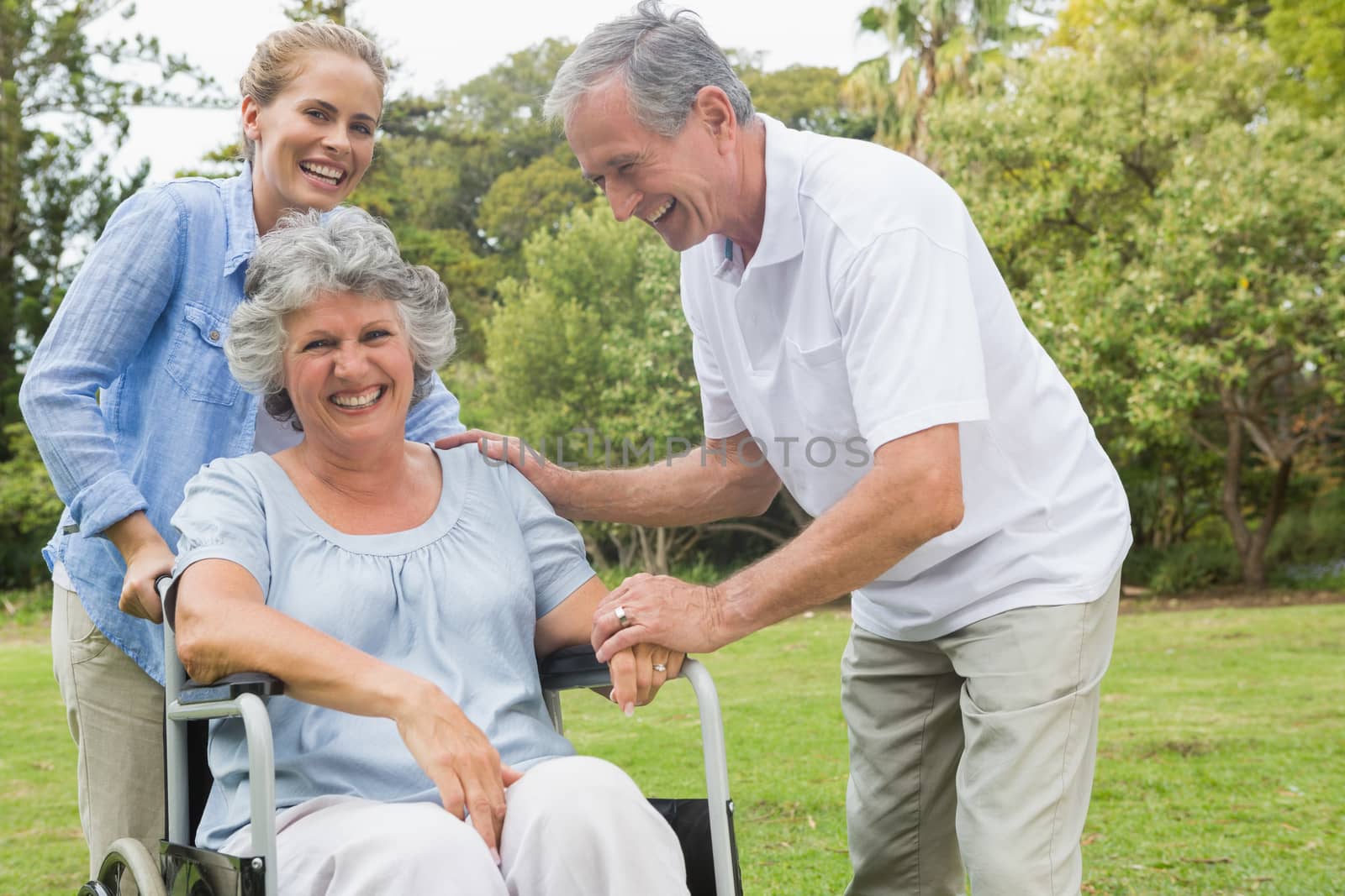 Happy woman in wheelchair with daughter and husband in the park laughing on sunny day