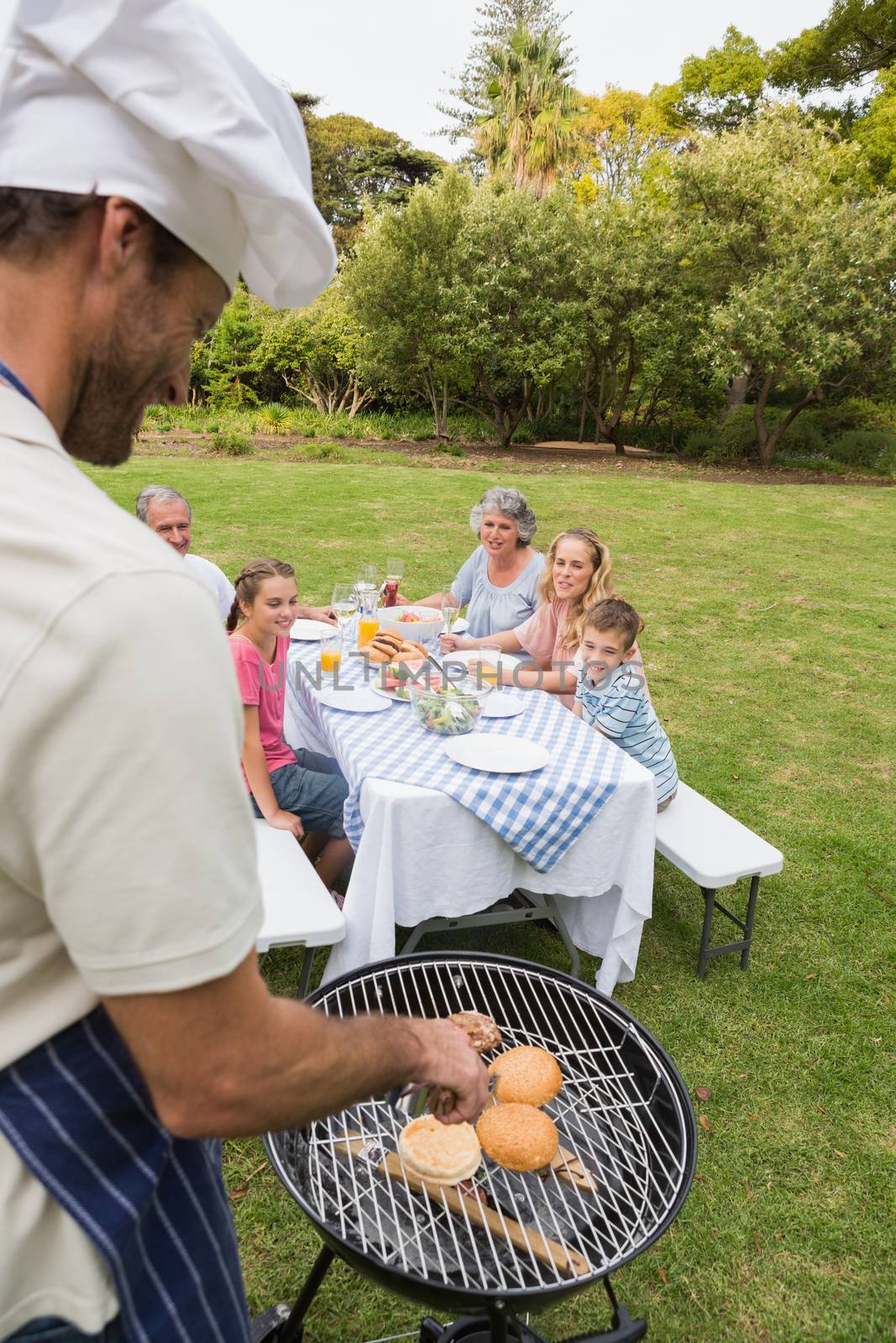 Smiling extended family having a barbecue being cooked by father in chefs hat by Wavebreakmedia