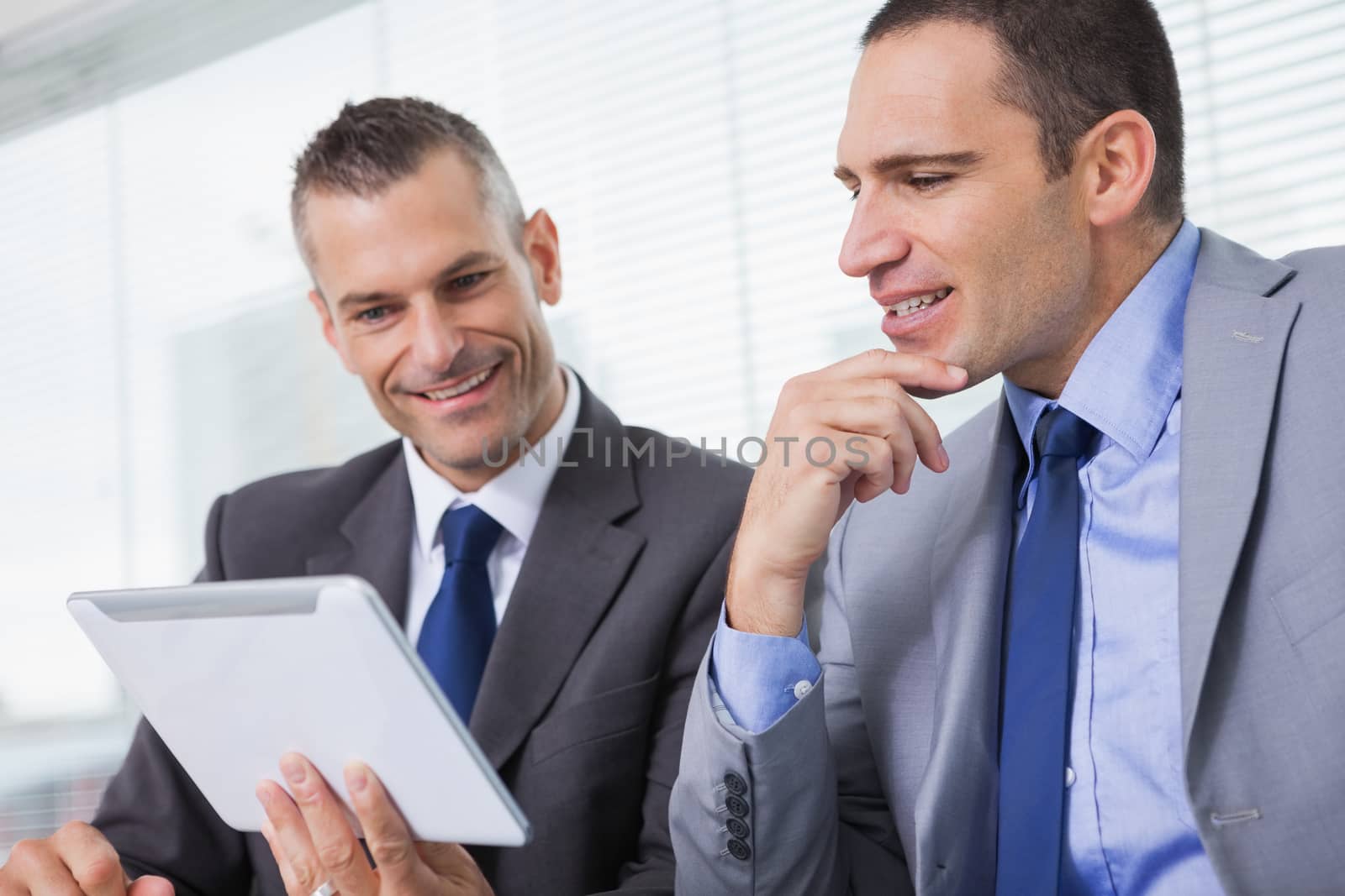 Smiling businessmen working together on their tablet in bright office