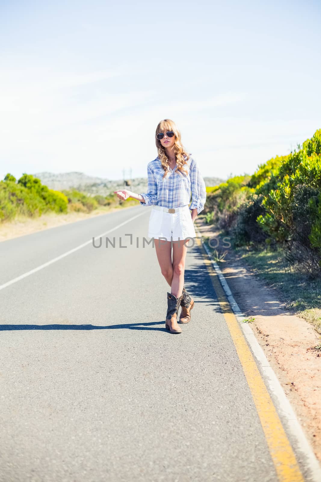 Trendy blonde with sunglasses hitchhiking on the roadside in the summer