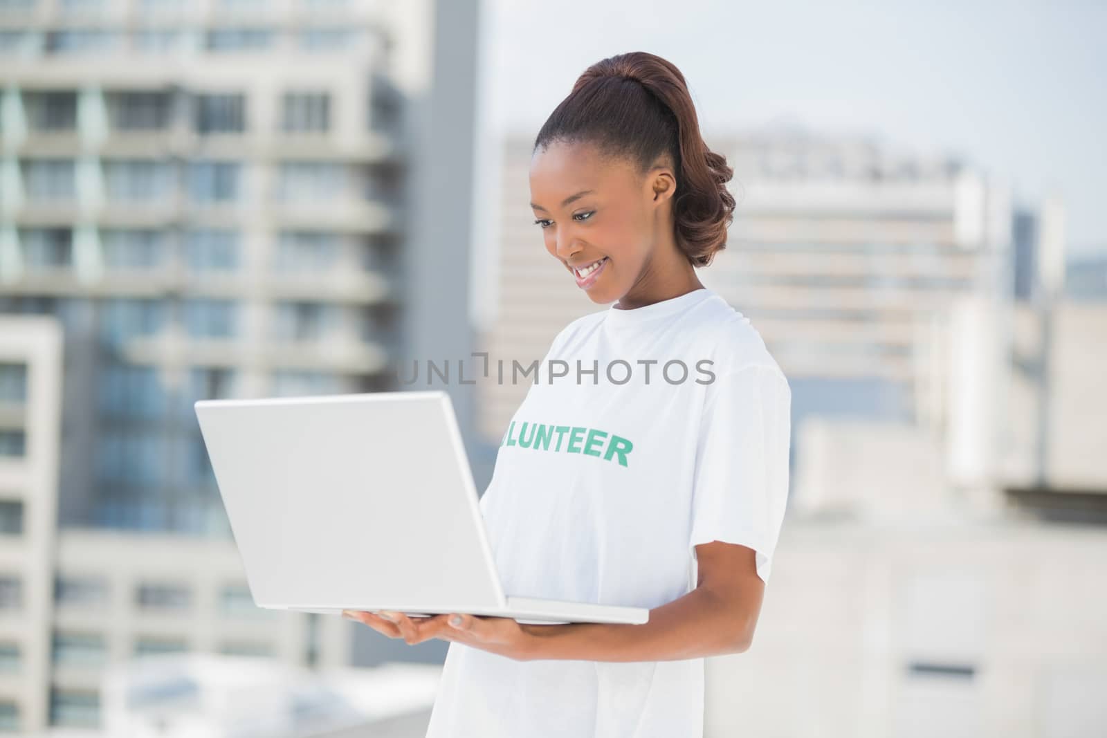 Smiling woman looking at her laptop outdoors on urban background