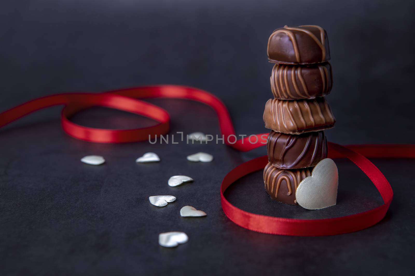Stack of Chocolate candy and red ribbon on a black background. Focus on chocolate.
