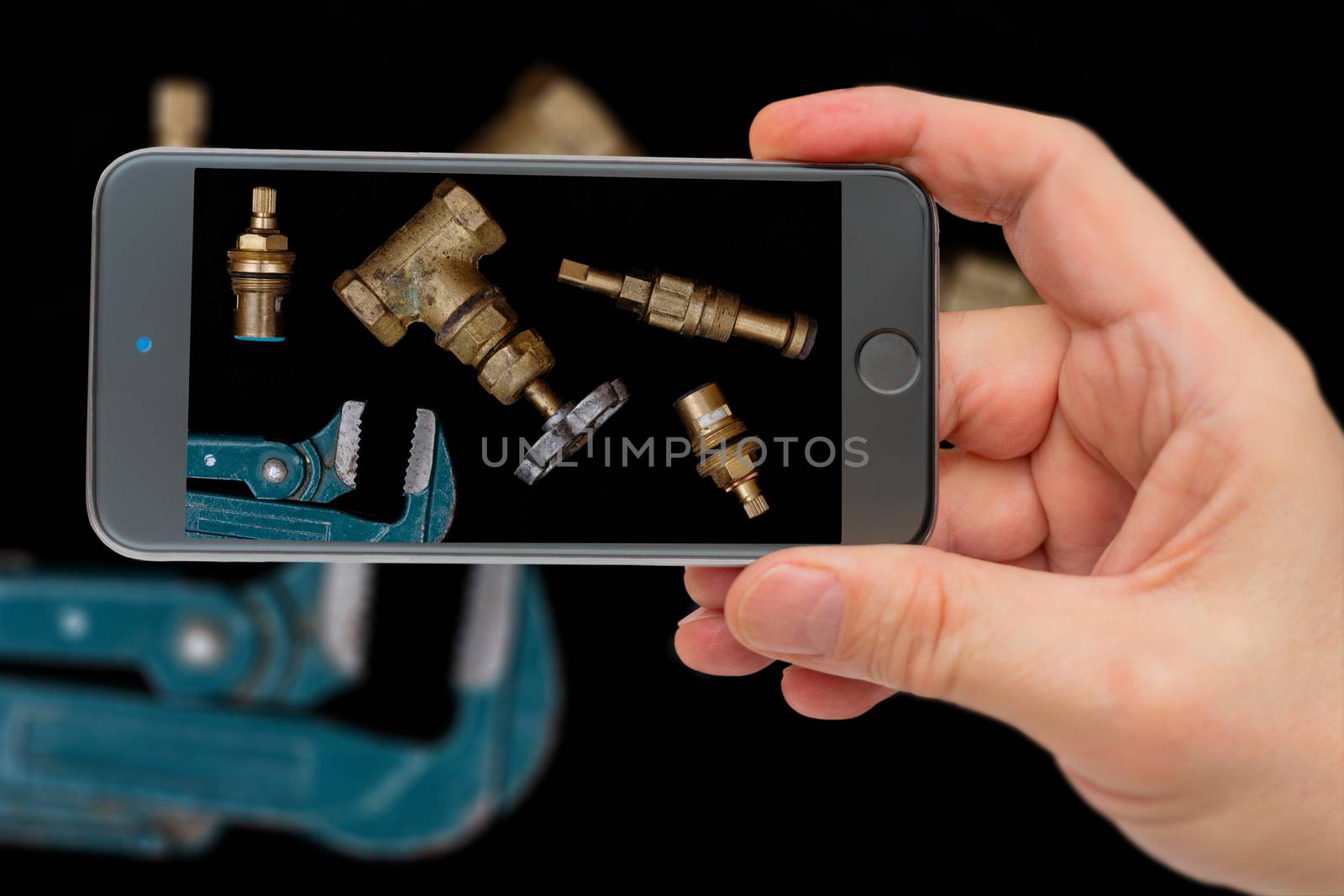 Plumbing tools on black background. Faucets, valve, pipe wrench to repair water supply system. Plumber tools on smartphone screen.