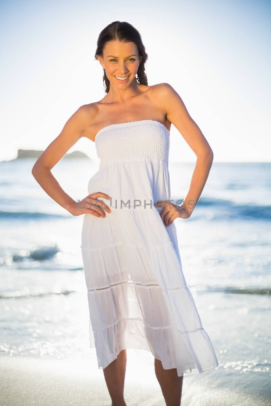 Smiling brunette in white summer dress posing on the beach at dusk