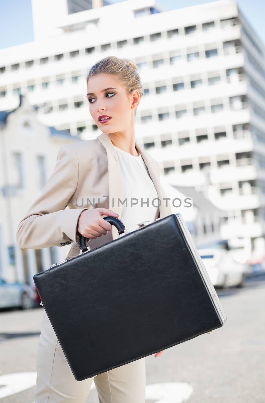 Serious elegant businesswoman holding briefcase outdoors on urban background