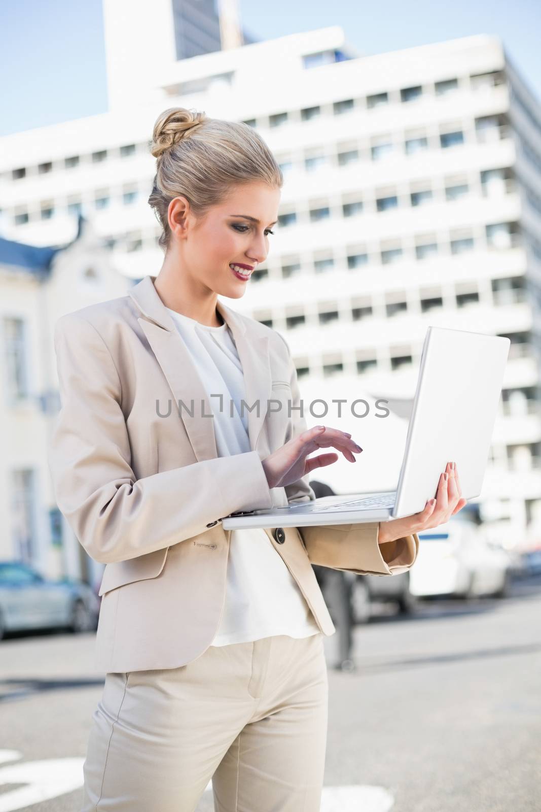Cheerful elegant businesswoman working on laptop outdoors on urban background