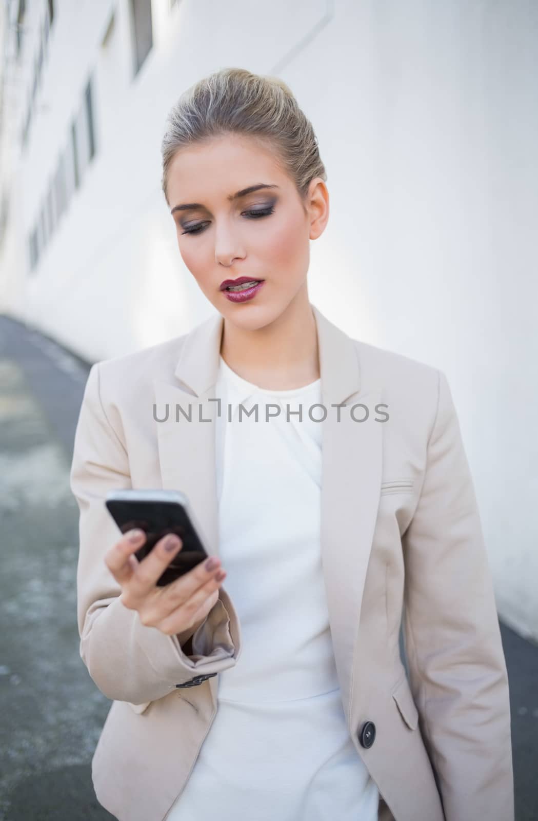 Serious attractive businesswoman sending a text outdoors on urban background