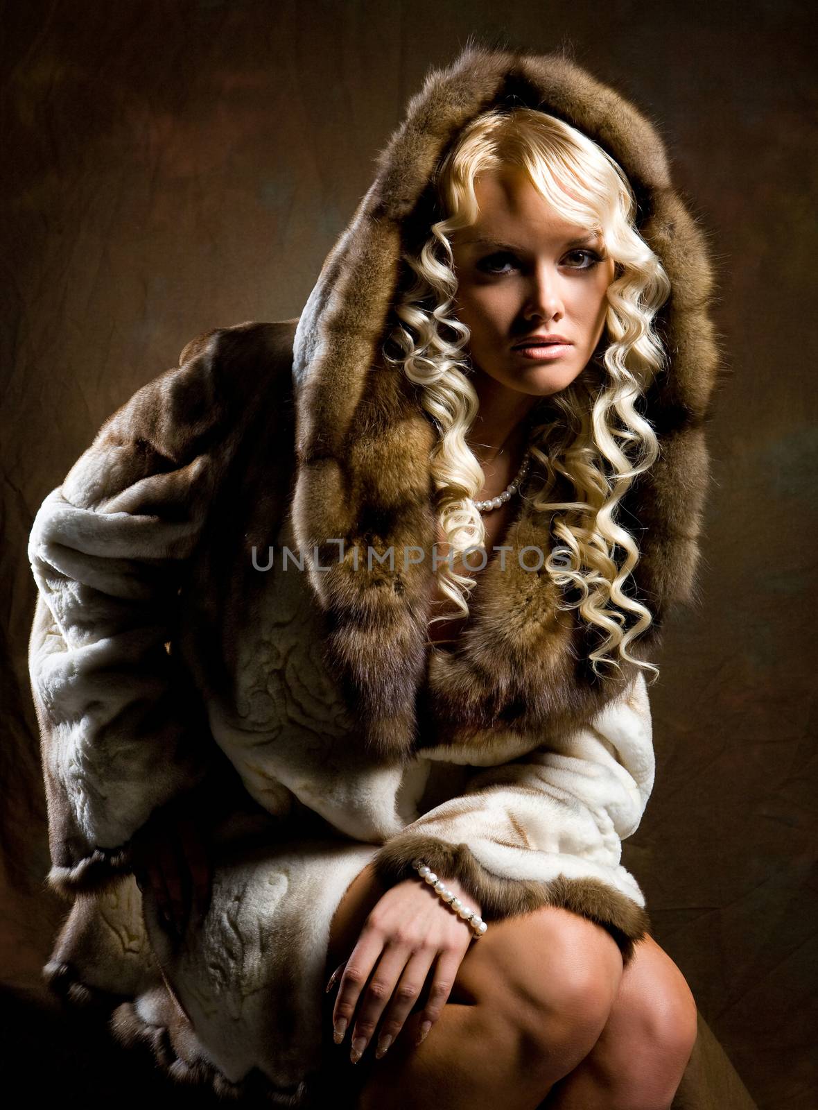 Young blonde woman in a fur coat on a studio background