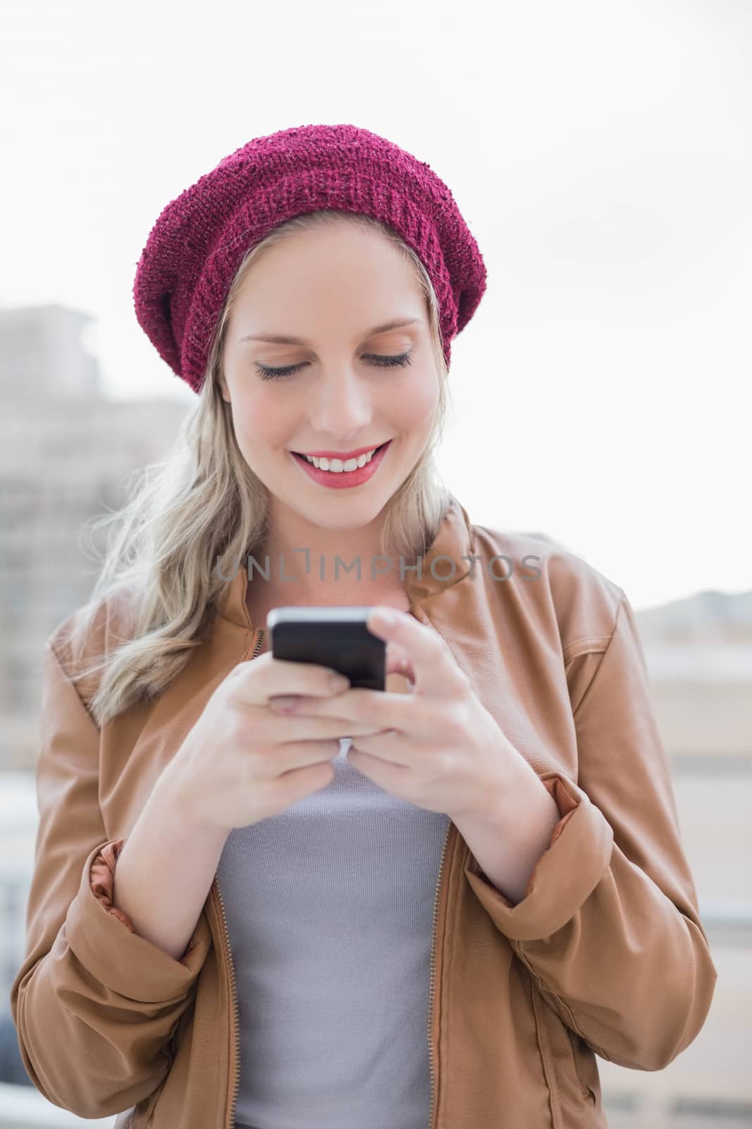 Smiling casual blonde text messaging outdoors by Wavebreakmedia
