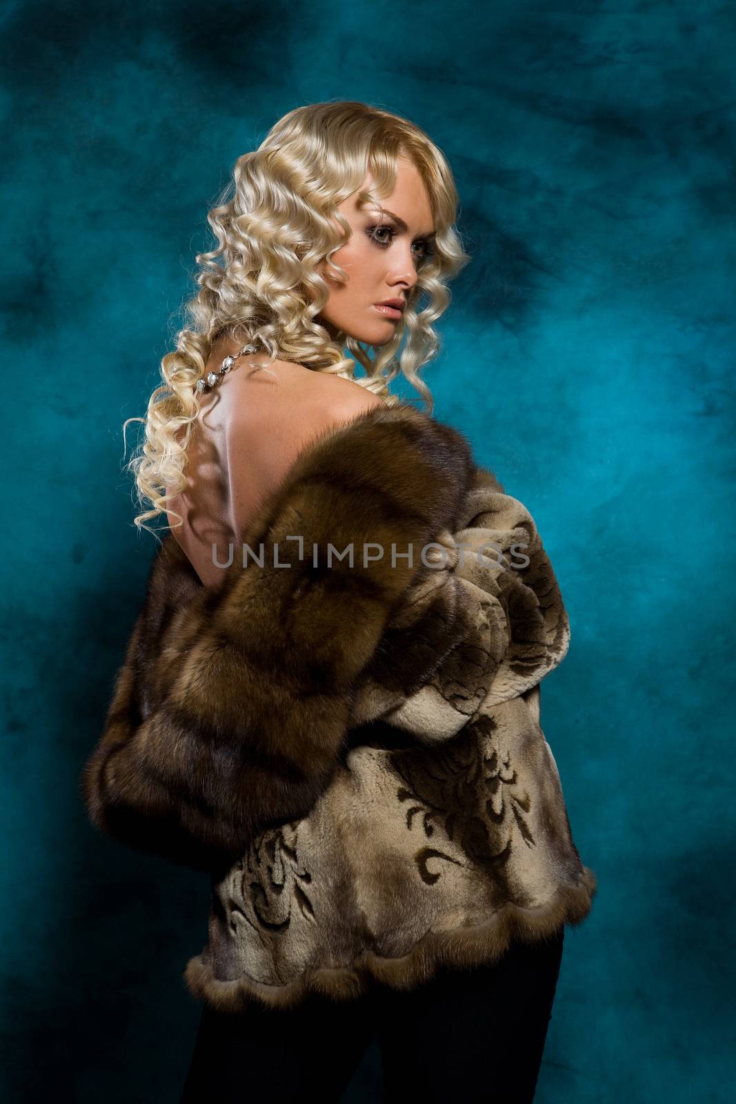 Young blonde woman in a fur coat on a studio background
