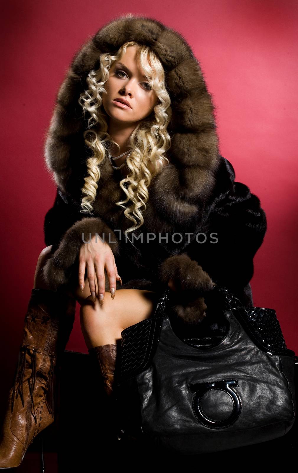 Young blonde woman in a fur coat on a studio background