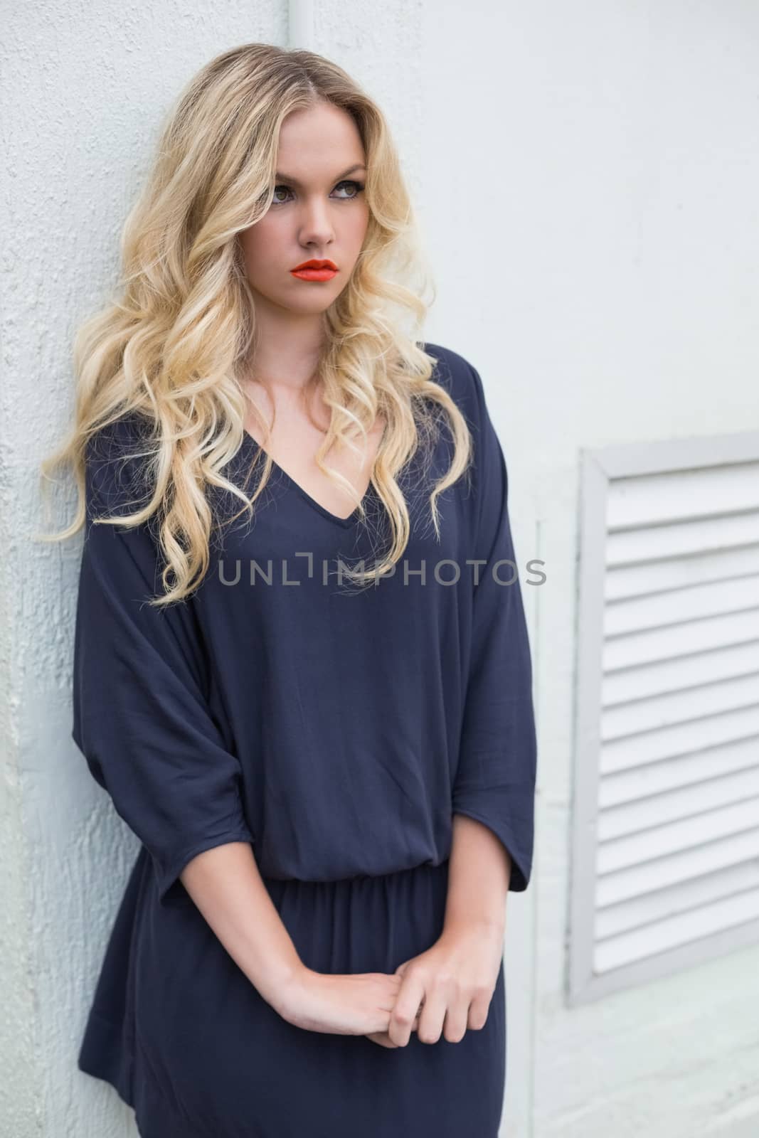 Thoughtful attractive blonde wearing classy dress outdoors against building