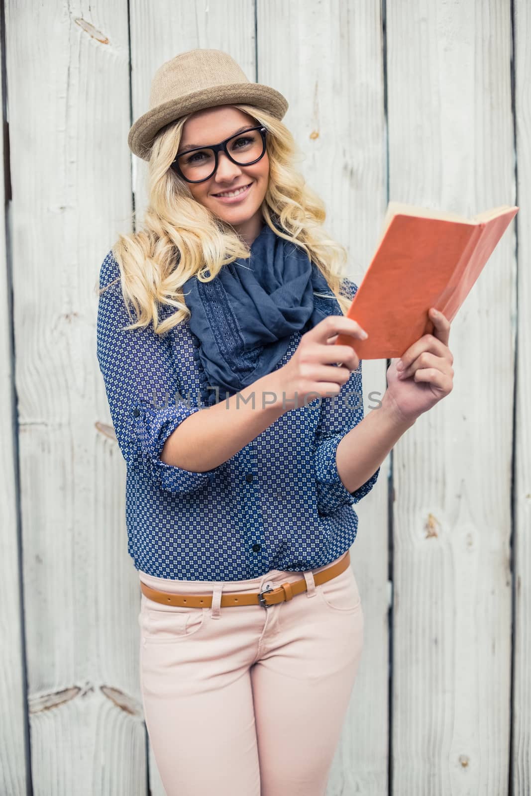 Smiling fashionable blonde holding book outdoors on wooden background