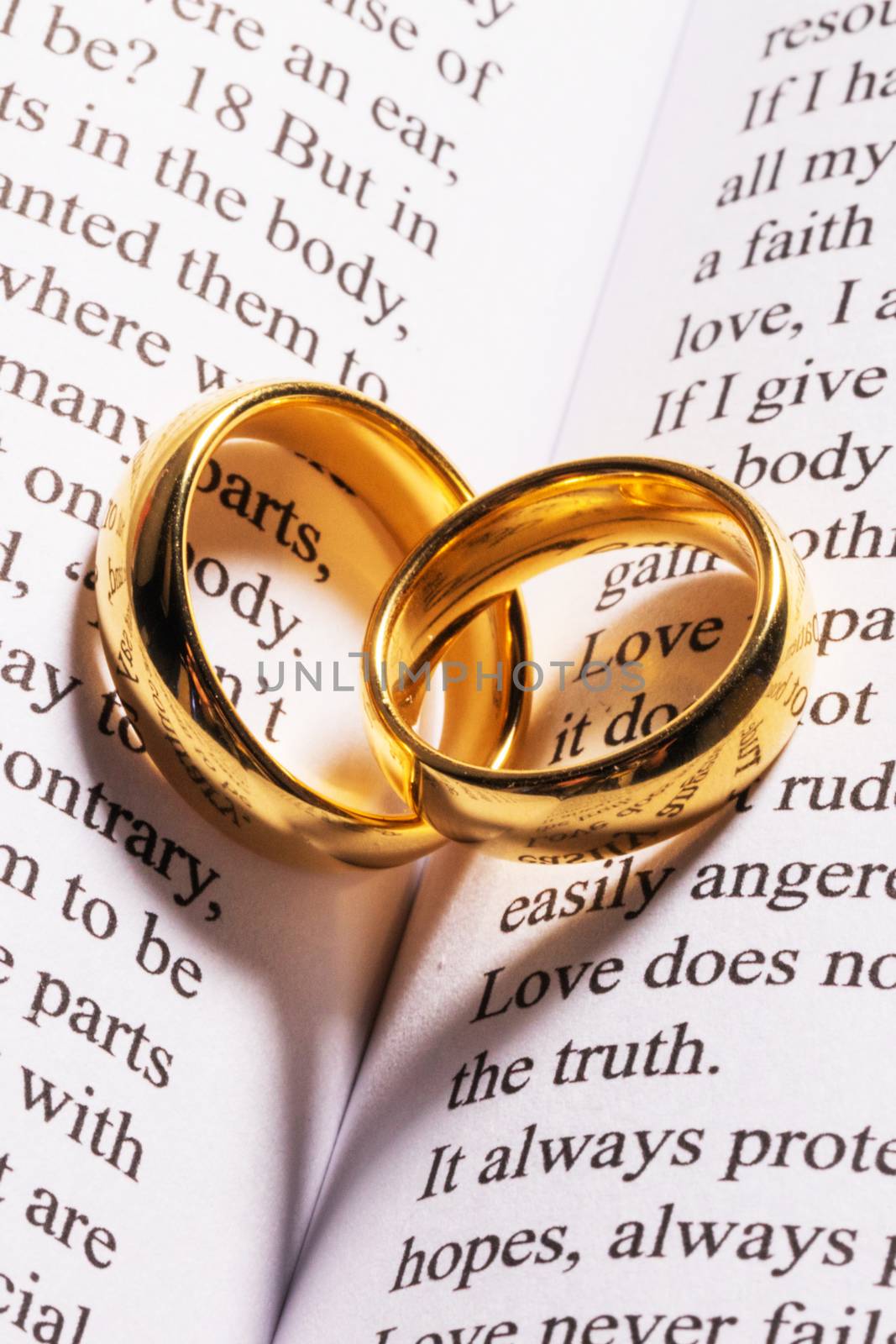 Two golden wedding rings on Holy bible book with heart shaped shadow close up