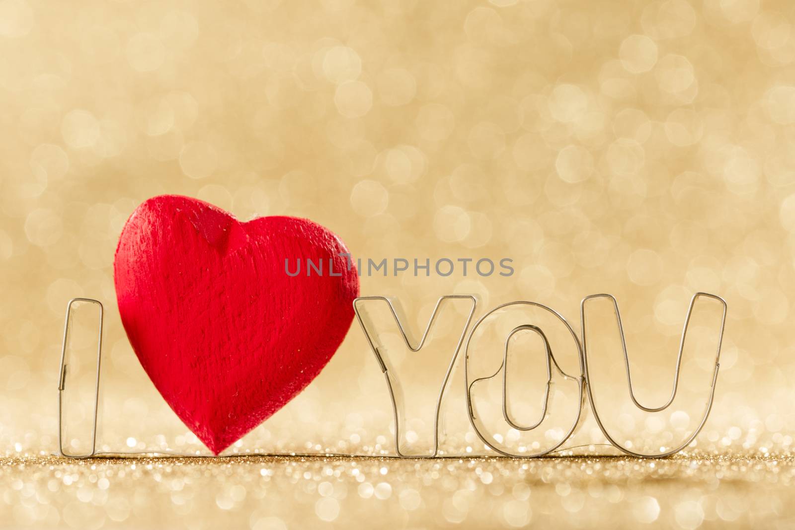 Red handmade wooden heart in I LOVE YOU sign word on golden bright glitter lights bokeh background