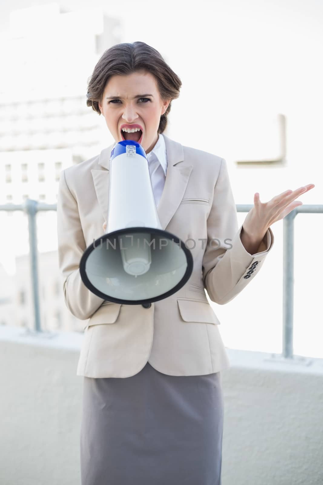 Angry stylish brown haired businesswoman yelling in a megaphone outdoors