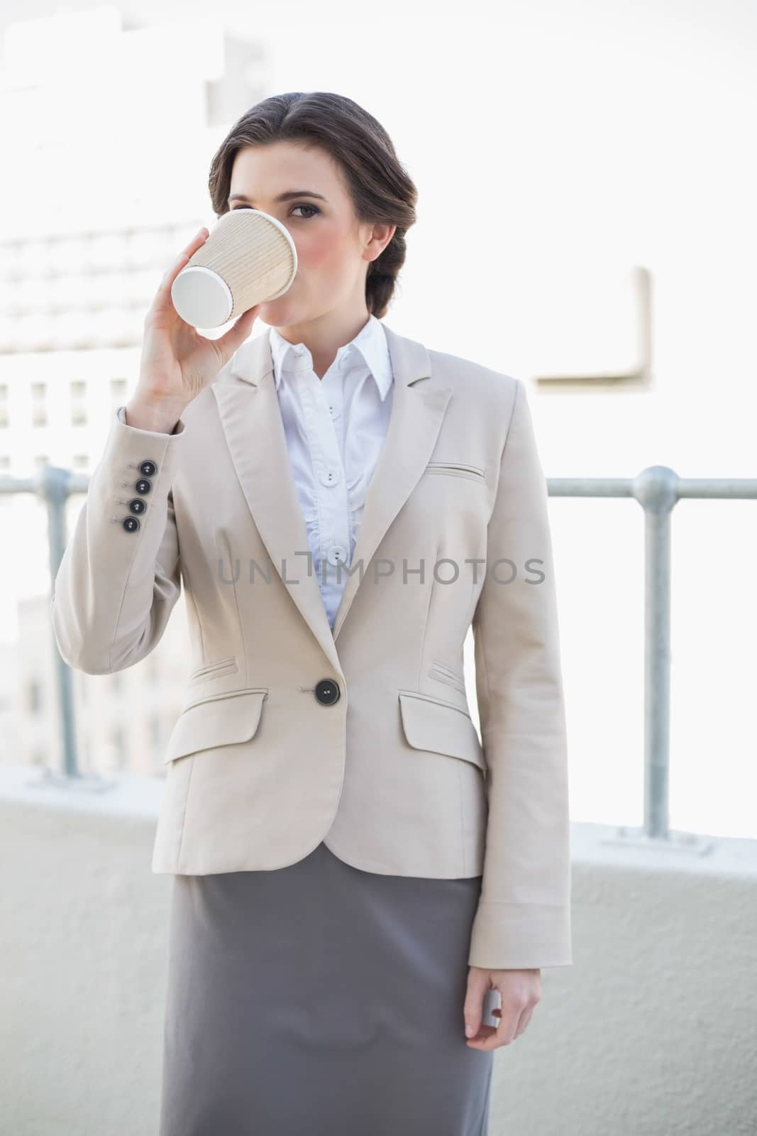 Calm stylish brown haired businesswoman drinking coffee outdoors