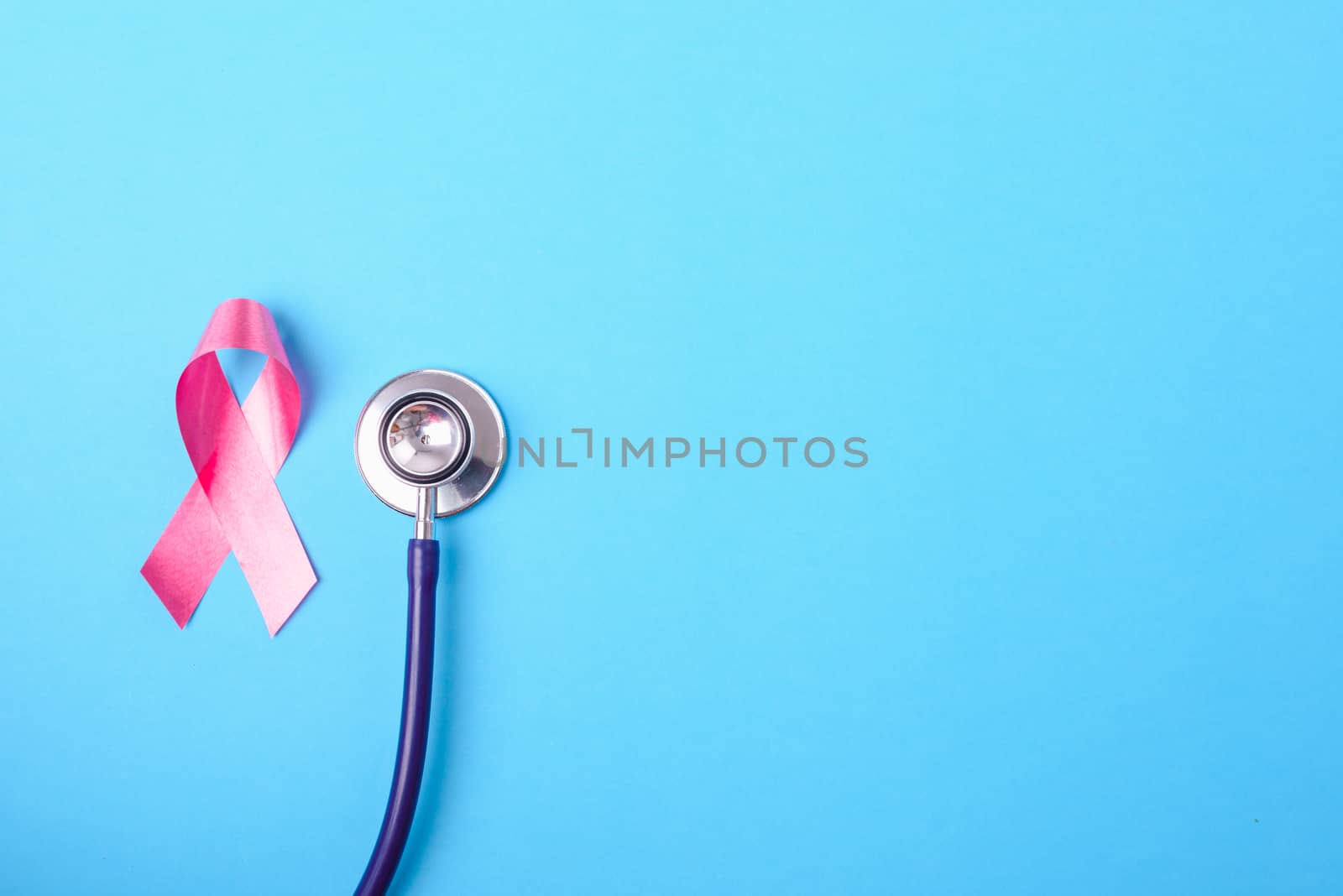 Breast cancer month concept, flat lay top view, pink ribbon and stethoscope on blue background with copy space for your text